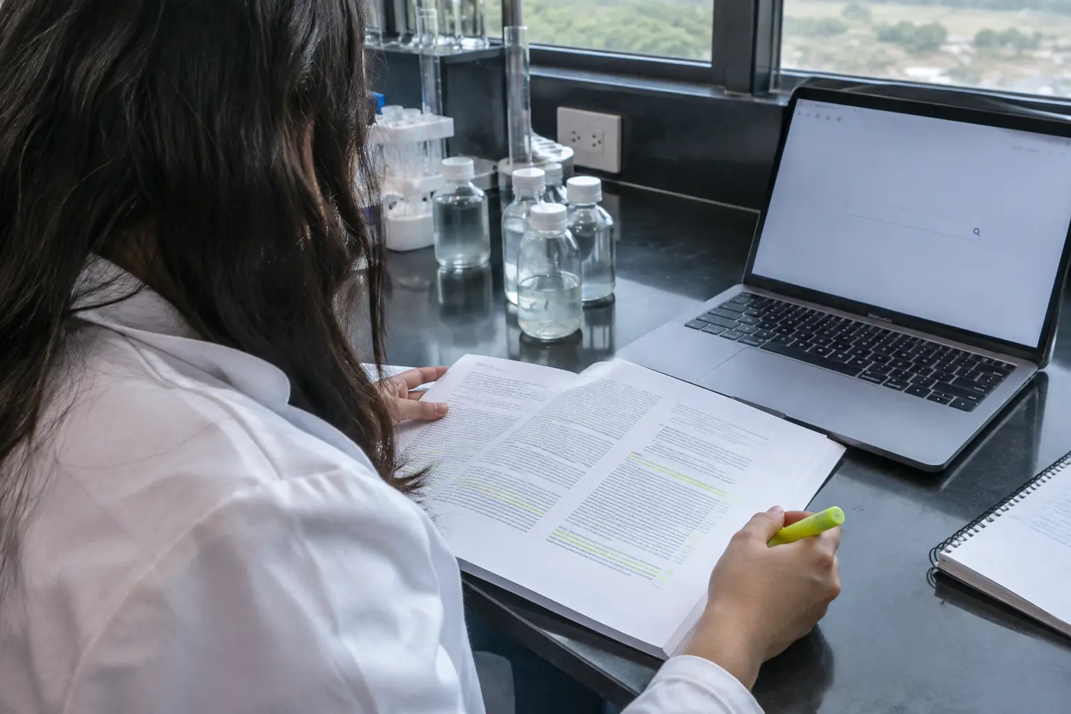 Estudiante de ingeniería ambiental leyendo un artículo científico junto a muestras de agua en el laboratorio