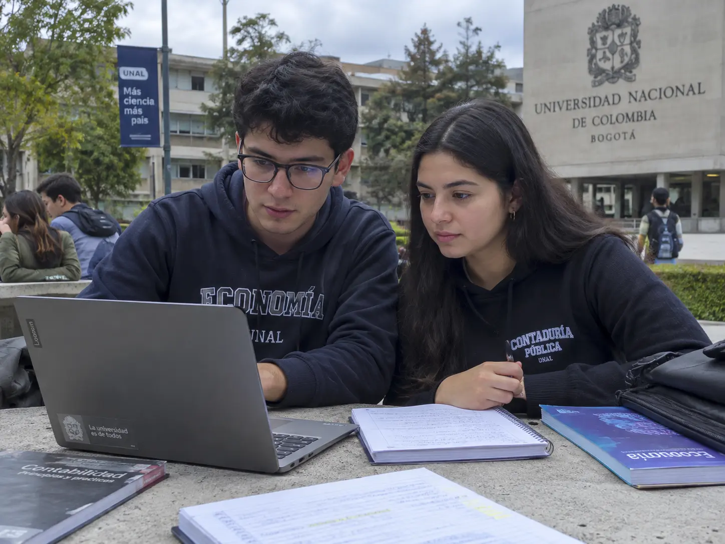 Estudiante revisando los acuerdos de trabajo de grado de su facultad en un portátil junto a un cuaderno